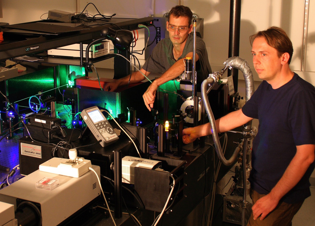University of Utah physicists John Lupton and Christoph Boehme use green and blue laser beams to "excite" a small piece of an organic or "plastic" polymer (glowing orange near Boehme's right hand) that may serve as a light-emitting diode (LED) for computer and TV displays and perhaps lighting.