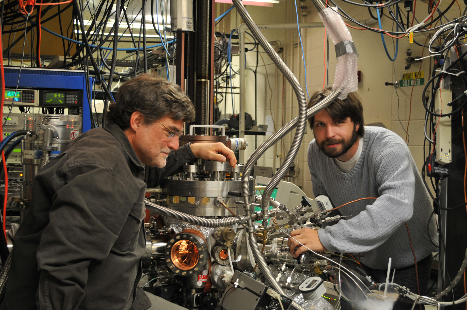 University of Utah chemistry Prof. Scott Anderson and doctoral student Bill Kaden work on the elaborate apparatus they use to produce and study catalysts, which are substances that speed chemical reactions without being consumed. The world economy depends on catalysts, and the Utah research is aimed at making cheaper, more efficient catalysts, which could improve energy production and reduce emissions of Earth-warming gases.